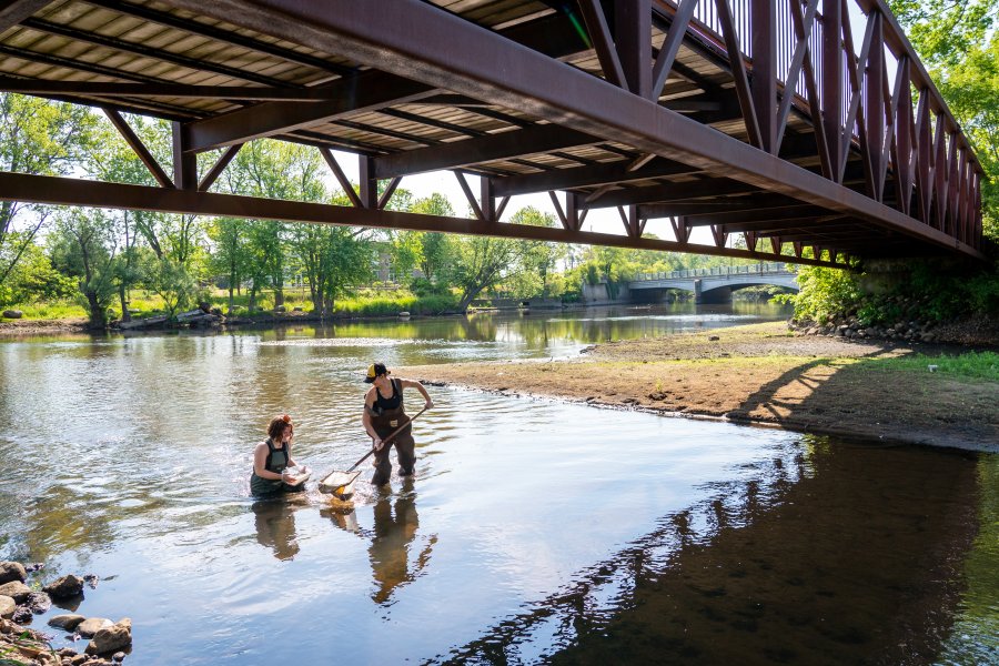 two students stand in a river taking a sample