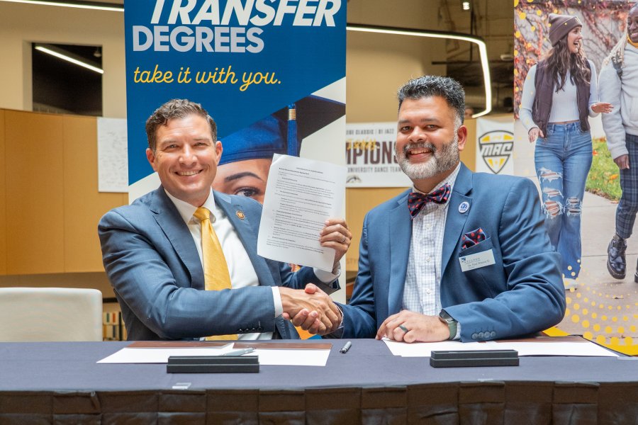 WMU President Russ Kavalhuna and KCC President Paul Watson II shake hands at a table.