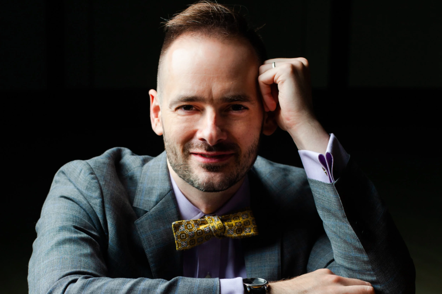 A smiling man in a light blue suit with a yellow bow tie.
