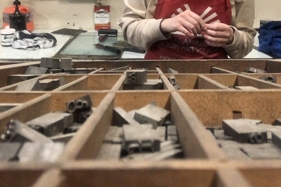 Painting alum Rachel Stickney in the studio wearing an apron behind a case of letters.