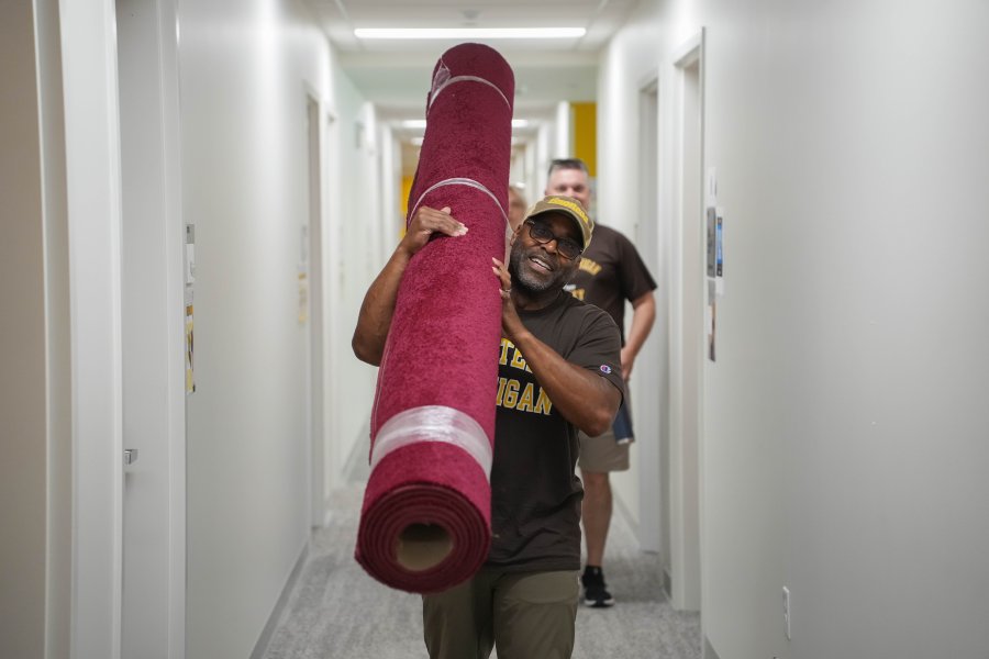 A dad carries a rug down a hallway.
