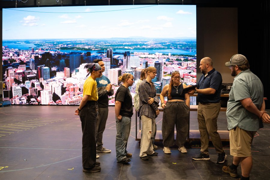 Students gather in a room next to a large LED screen.