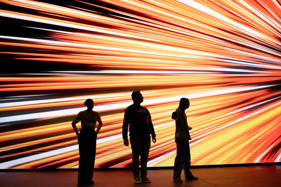 Students stand in front of a vibrant image on a large LED screen.