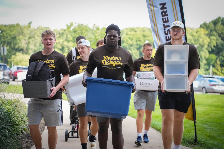 Student-athletes carry bins into a residence hall.