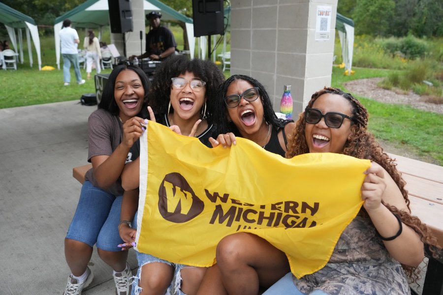 Happy students hold a gold Western Michigan University flag.