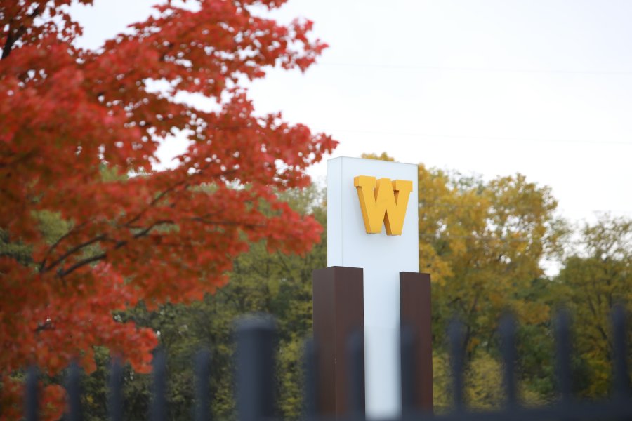 Western Michigan University’s W logo on a Main Campus sign surrounded by fall foliage.
