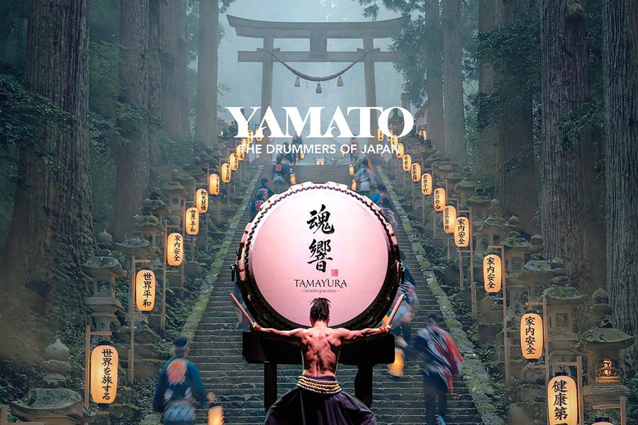 Promotion image of YAMATO: The Drummers of Japan featuring a taiko drum at the base of a lantern-lined staircase. A drummer stands before the drum with arms outstretched.
