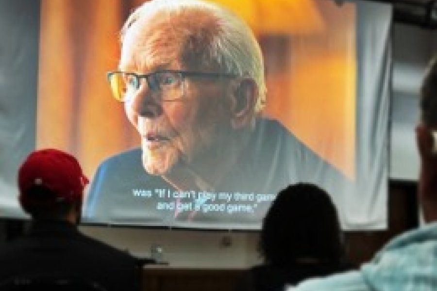 Audience looking at movie screen projecting older man from documentary film