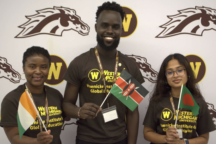 A group of orientation leaders pose behind a Bronco backdrop at International Student Orientation. They hold flags from their home countries.