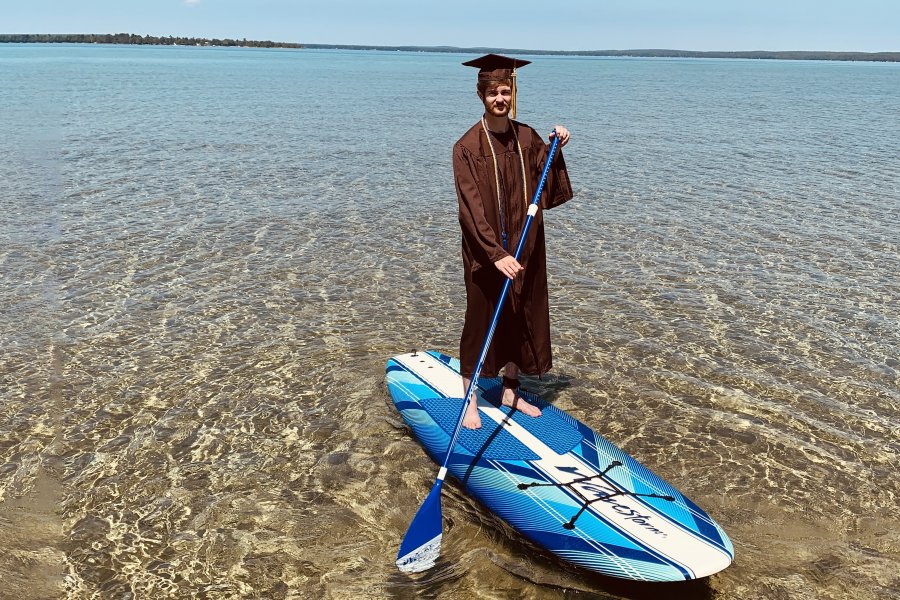 RJ Bolzman stands on a paddleboard in his cap and gown.