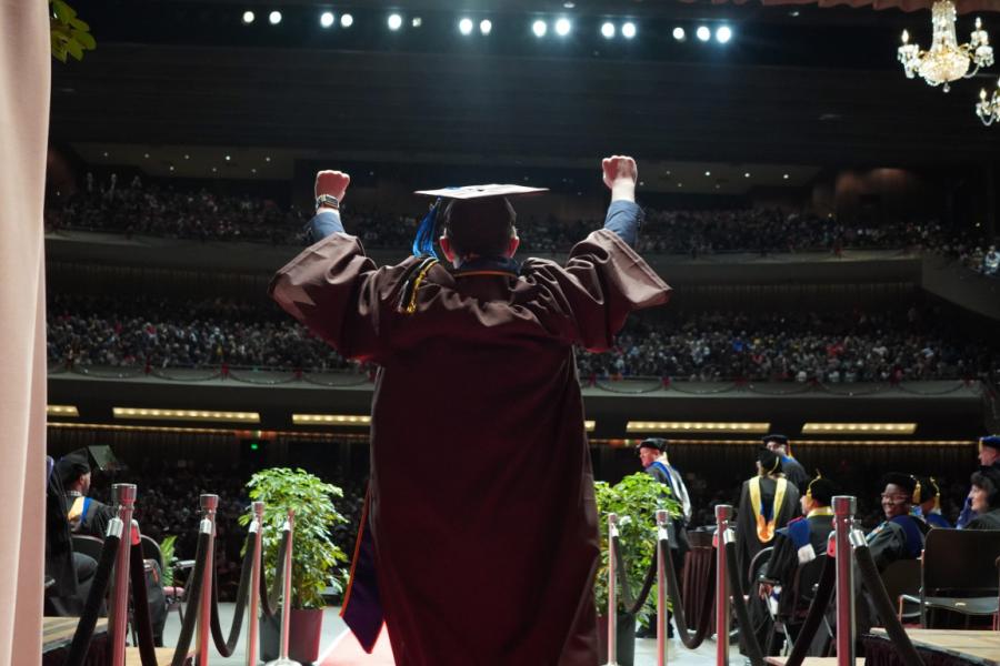 A graduate holds his arms up as he walks onto the stage.
