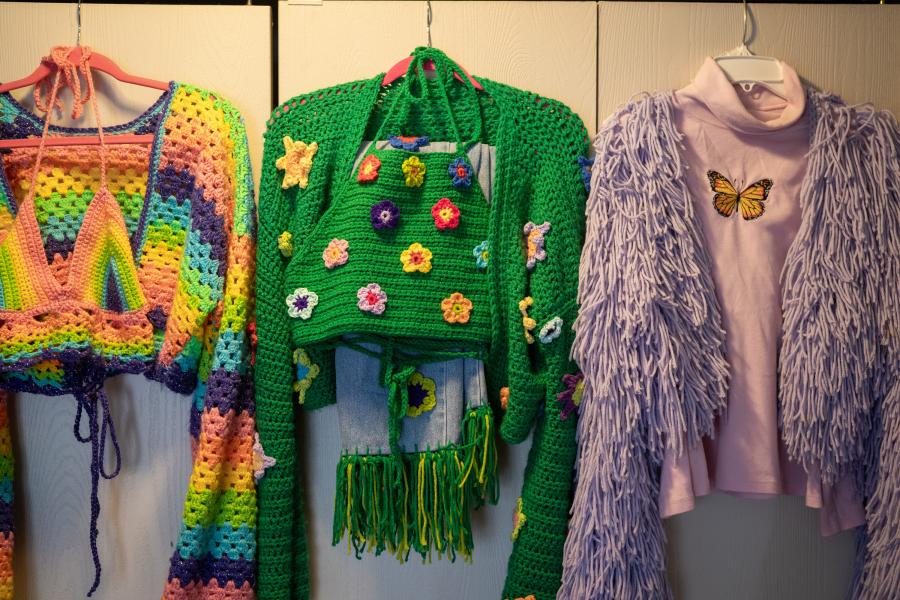 Several crocheted outfits on hangers.