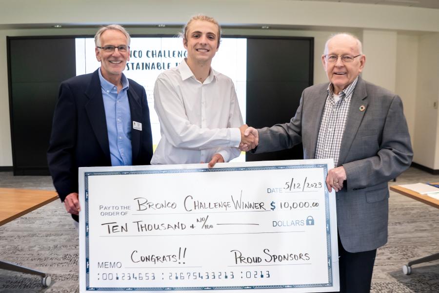 Three people hold a large check and shake hands.