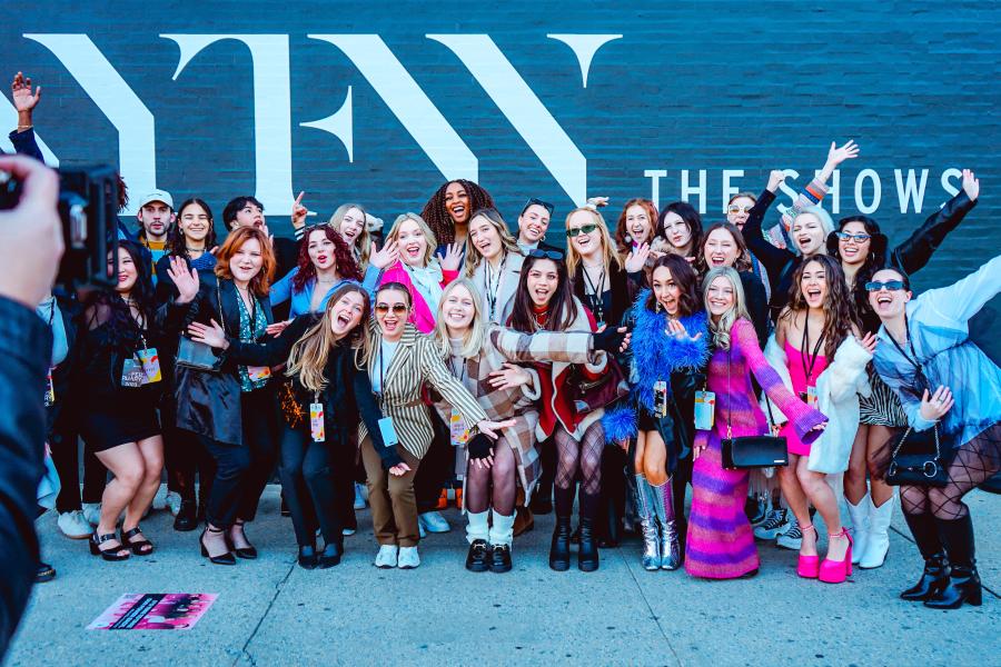 A group photo in front of a black wall with the letters "NYFW."