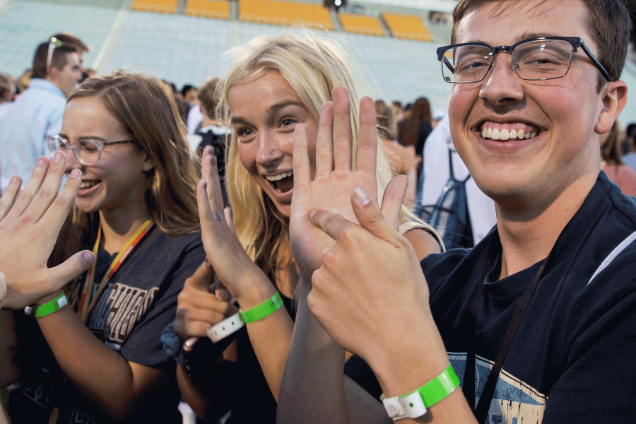 Students at Fall Welcome Stadium Night using their hand to point at where in Michigan they're from, smiling.