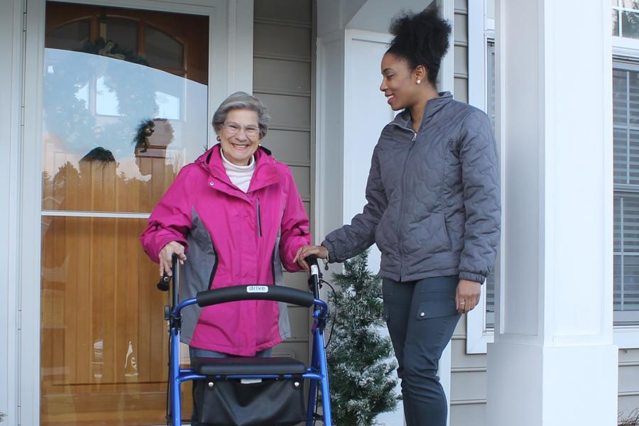 student staff assisting senior woman out of home