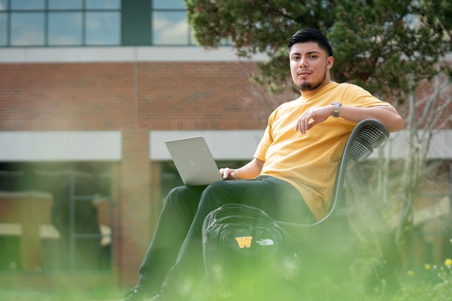 Male student on a bench with computer.