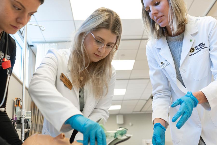 A nursing student practicing on a dummy with an instructor watching.