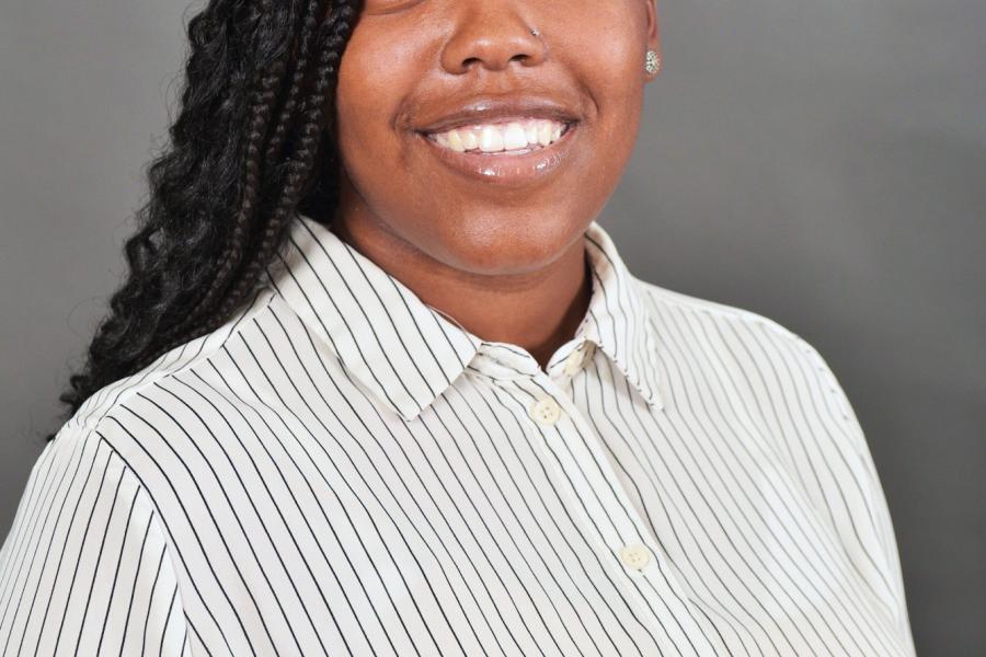 Shontiana Jackson is smiling and wearing a light-colored striped shirt.