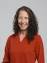 Christine Hassing in an orange shirt, dark curly hair is down and she is smiling 