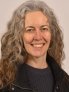 A woman with gray curly hair smiling wearing a black shirt and jacket.