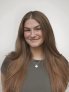 Amelia Perleberg is wearing a gray shirt and smiling in front of a white background. 