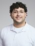 Ridha Chehime smiles for a formal portrait against a light background. He is wearing glasses and a white polo shirt.