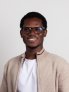Godfred Oppong head and shoulders wearing a tan jacket and a white shirt with glasses