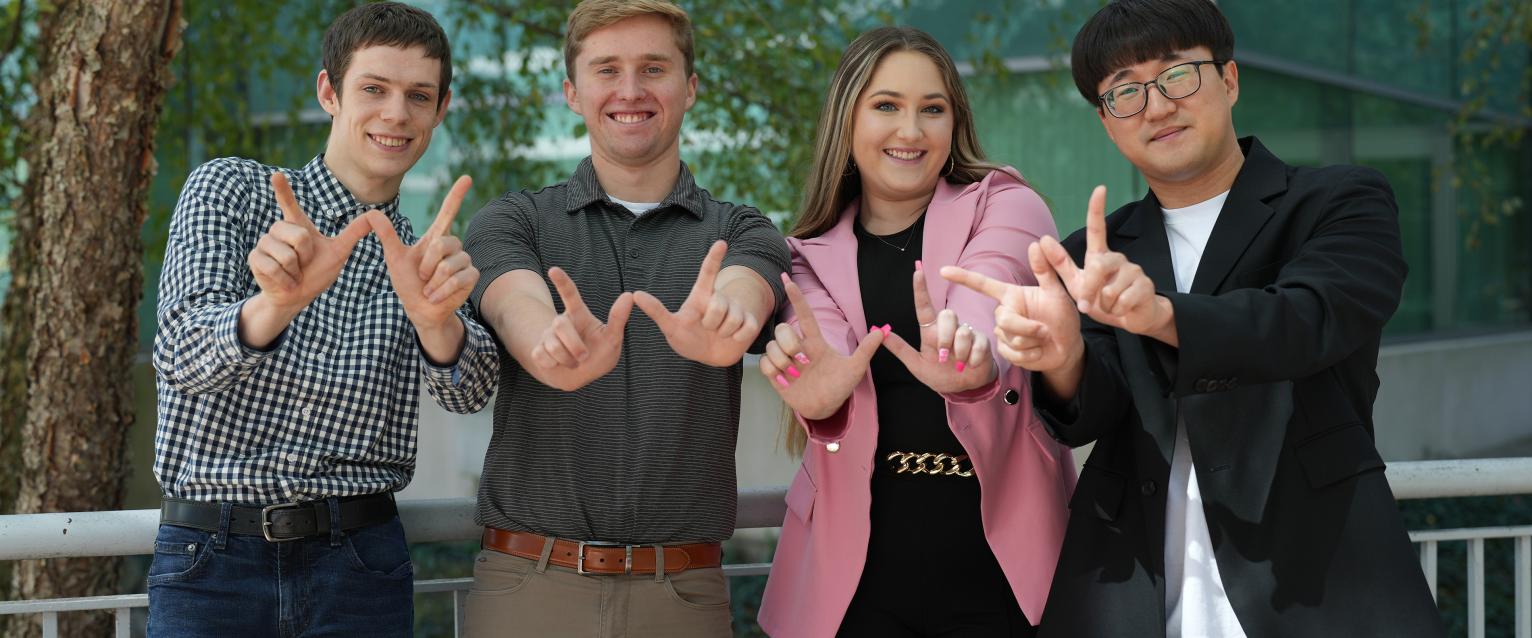 Four students in professional dress flashing the W