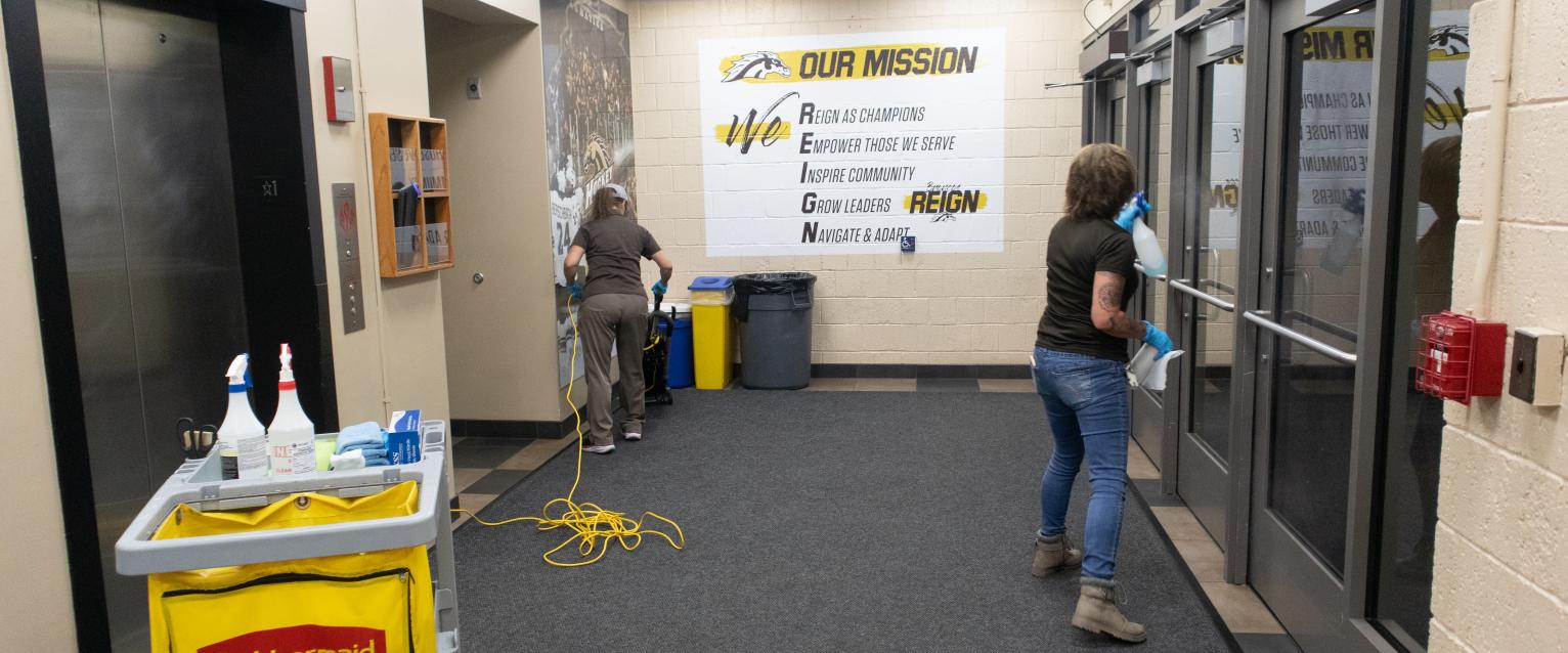A custodian is seen changing the trash bag for a trash bin near the entrance of University Arena.