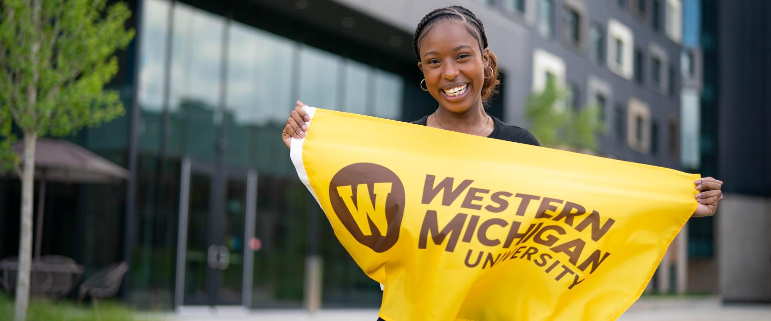 Female outside of Arcadia Flats holding a WMU gold flag