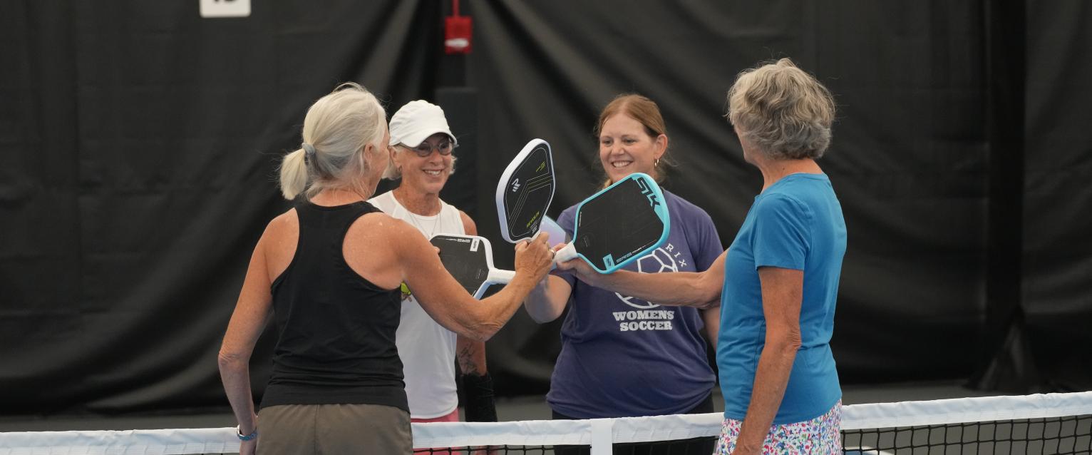 Four ladies at the net clicking their pickleball paddles