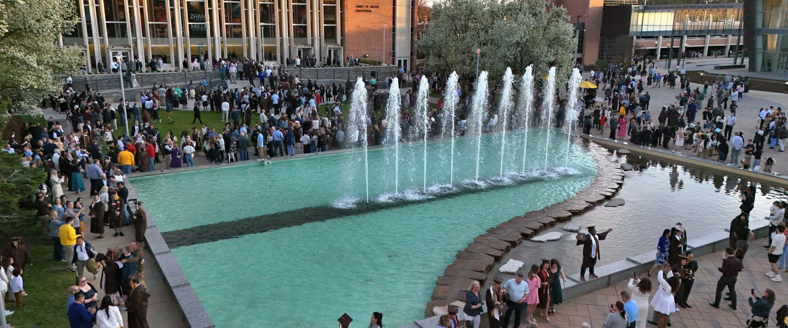 Miller Fountain plaza is seen after a spring 2025 commencement ceremony, with graduates and their guests gathering in the plaza for pictures and celebration. Miller Auditorium can be seen in the background.