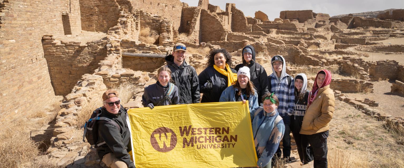 Desert Southwest students hold a WMU flag in front of Pueblo dwellings.