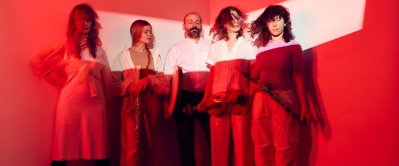 photo of five musicians standing in front of a red background