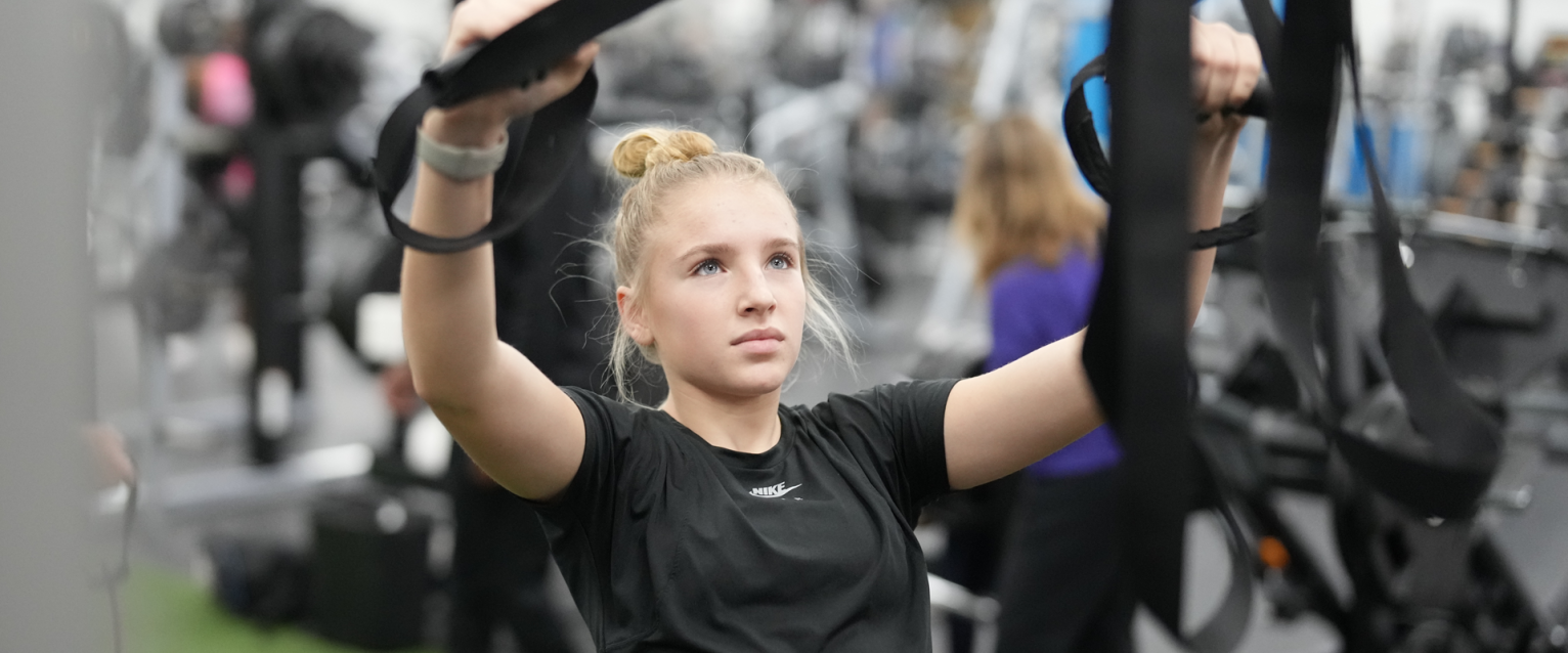 Girl pulling herself up by black straps at the gym