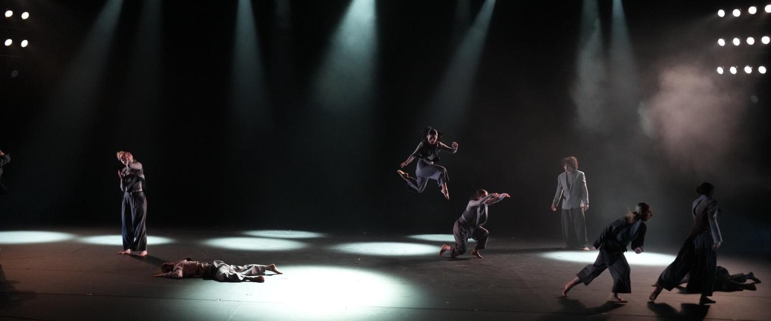 Image of dark stage with spotlights on multiple dancers in dynamic poses.
