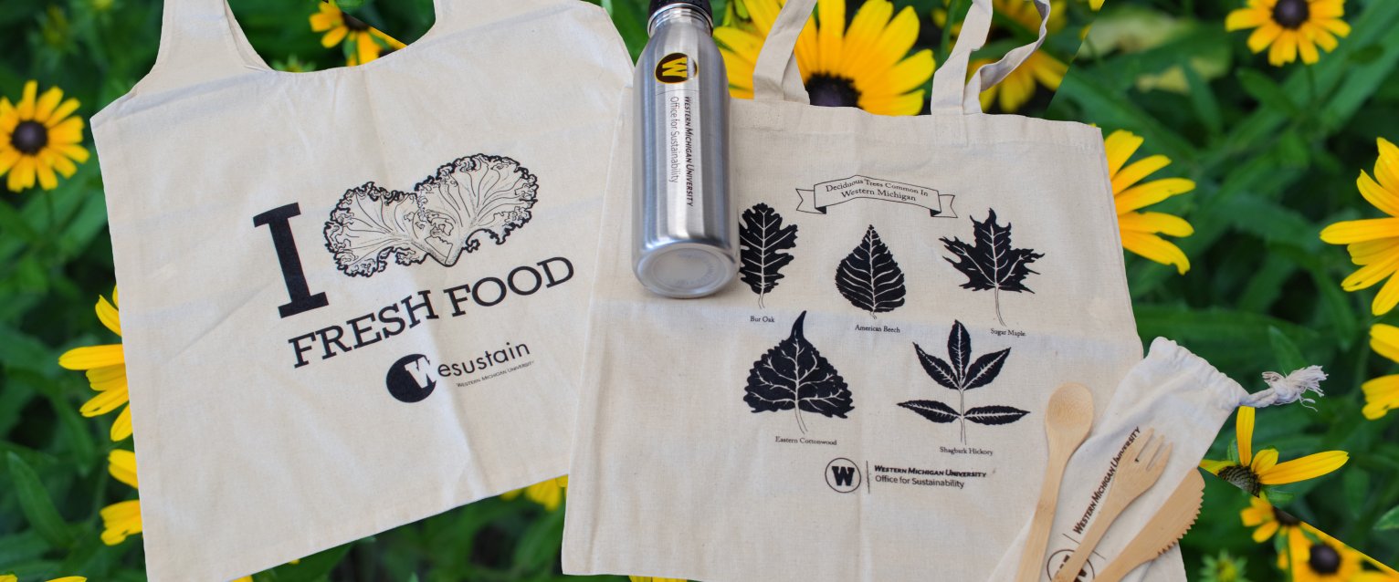 Image shows two tote bags, one water bottle and bamboo utensils. The background is black eyed susans.
