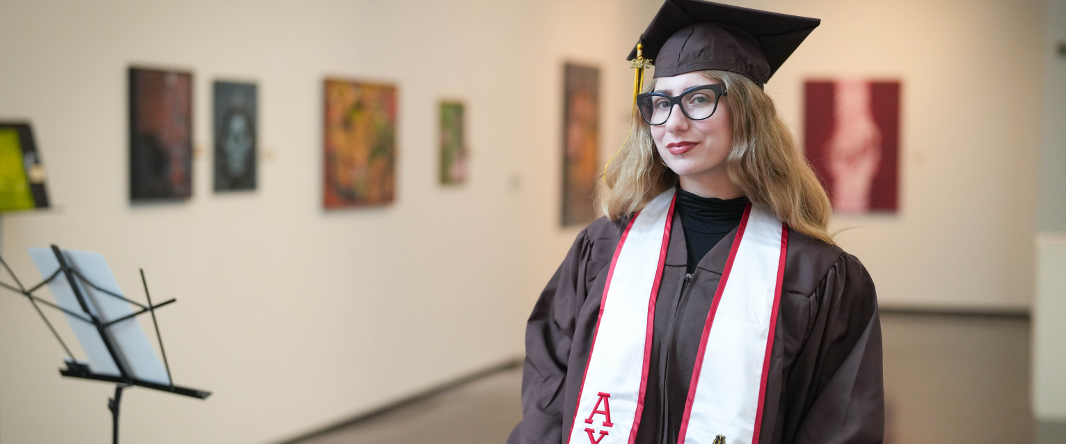 Hope Donovan poses for a portrait in her graduation cap and gown inside an art gallery.
