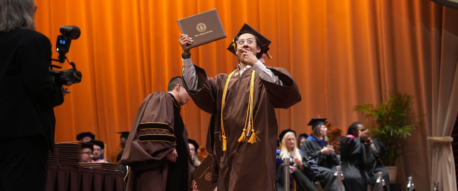 A graduate points to his diploma as he crosses the commencement stage at Miller Auditorium