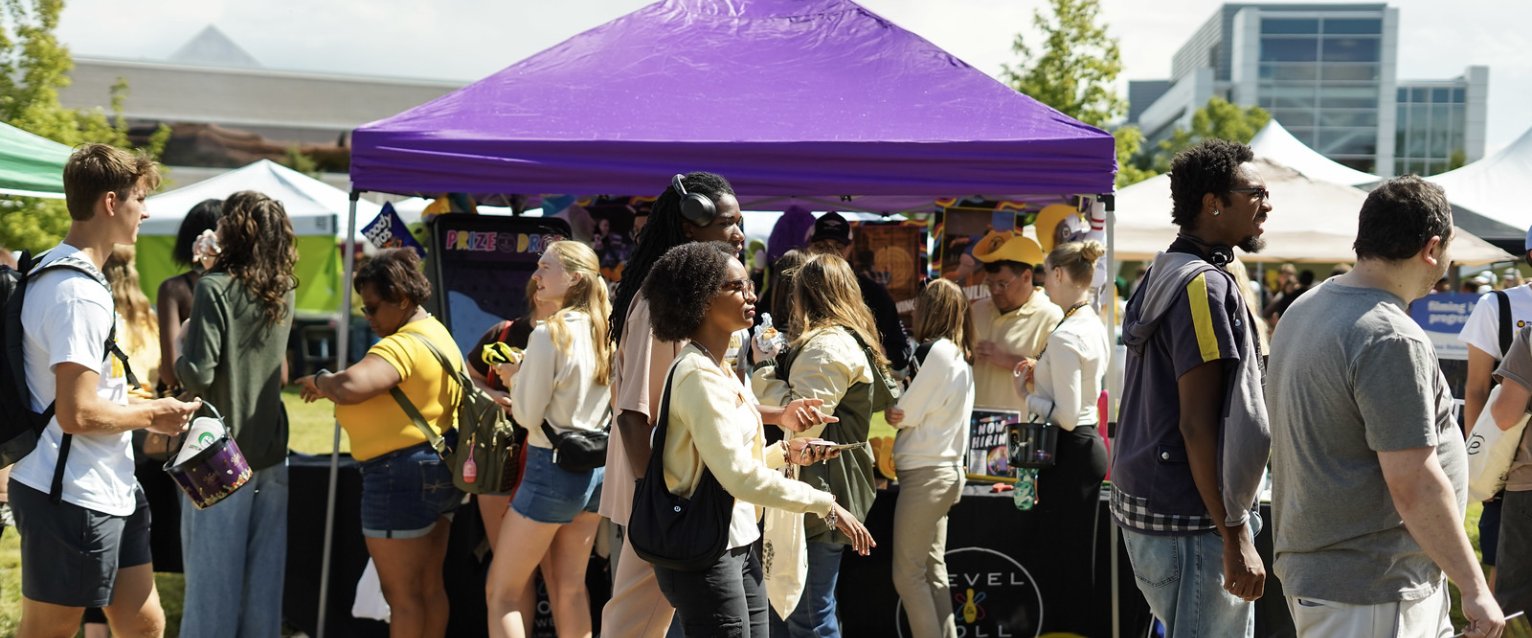 Various students walking by info tables outside during Bronco Bash.