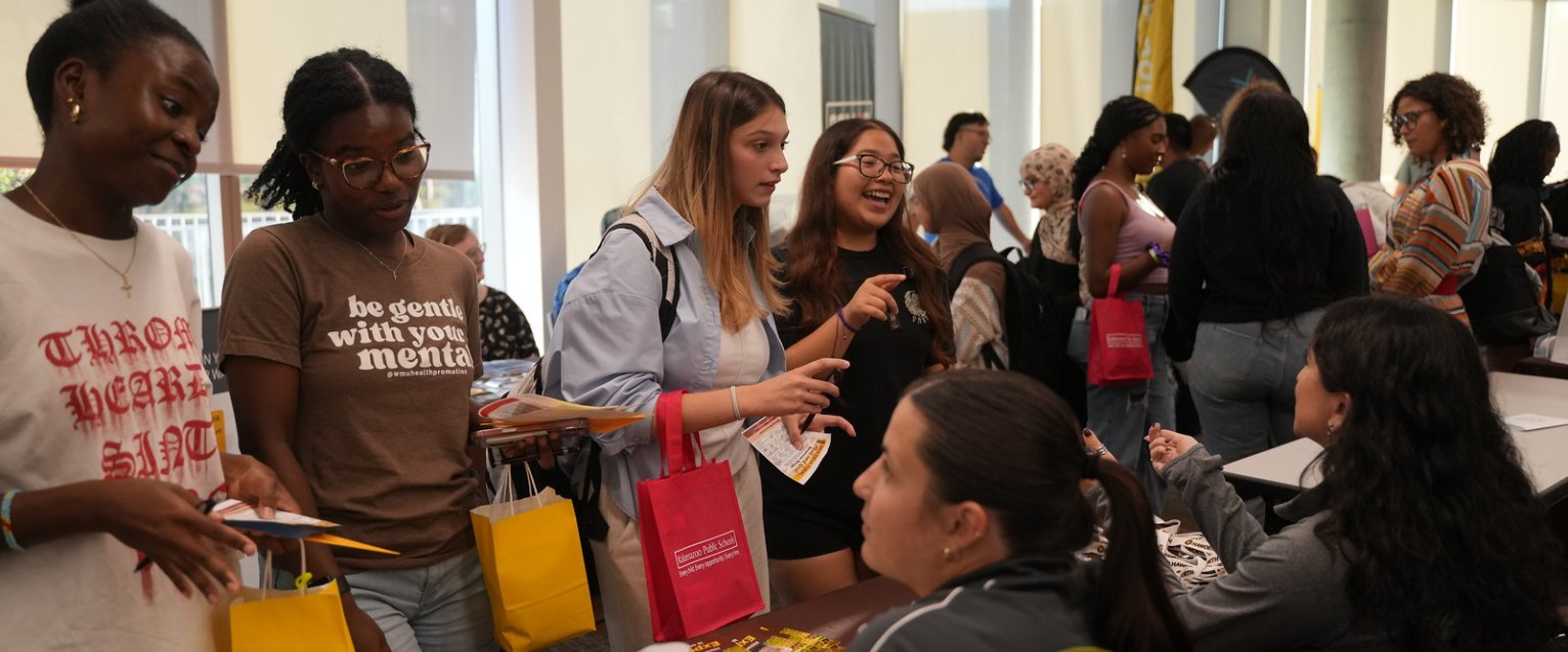 Two groups of students talking to representatives behind an information table at Multicultural Meet and Greet.