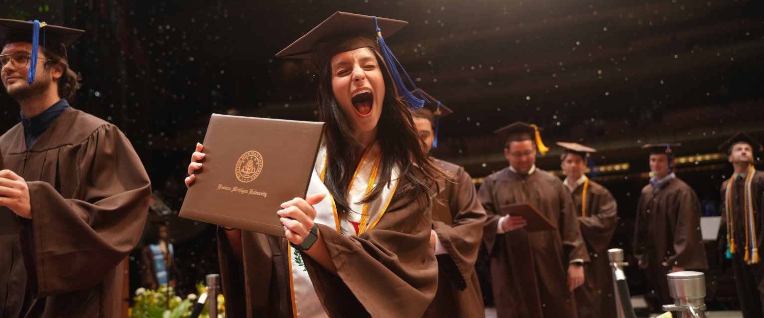 a 2024 Western graduate holds up her diploma excitedly as she crosses the commencement stage