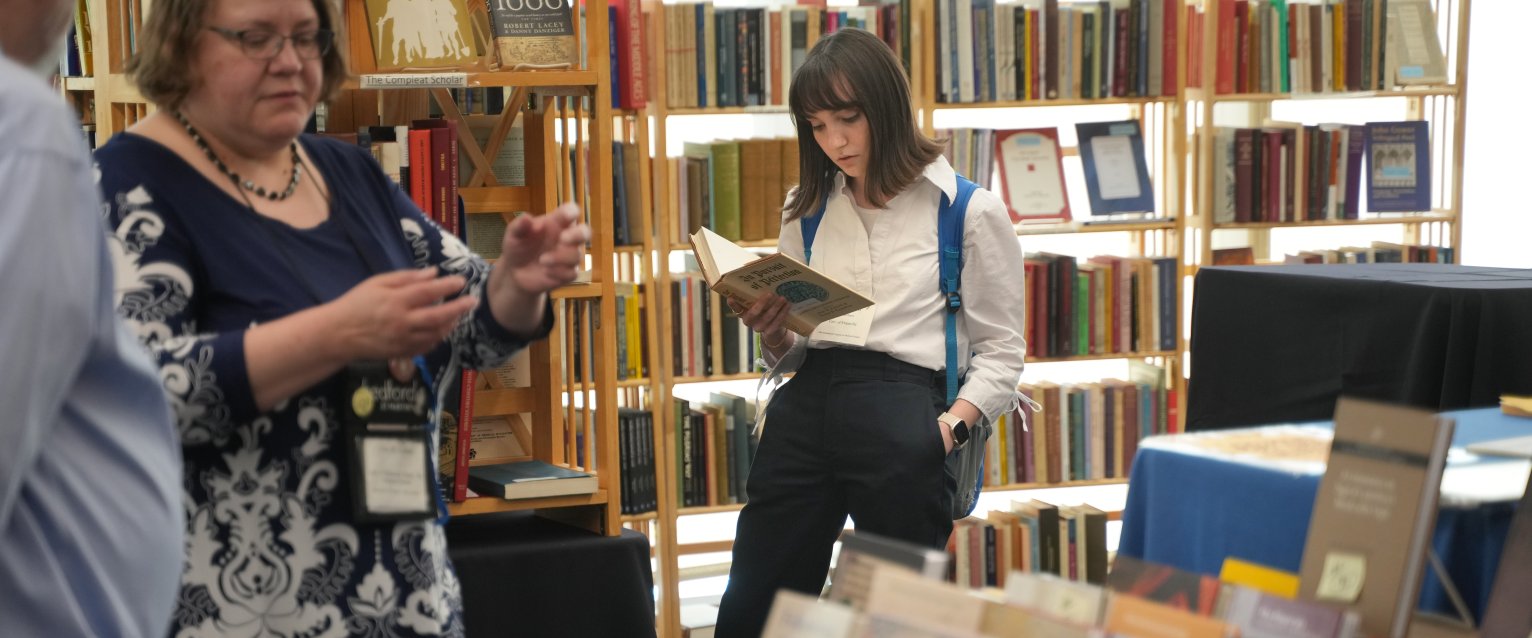 Person with mid-length brown hair, wearing a white collared shirt and dark slacks, reading a book.