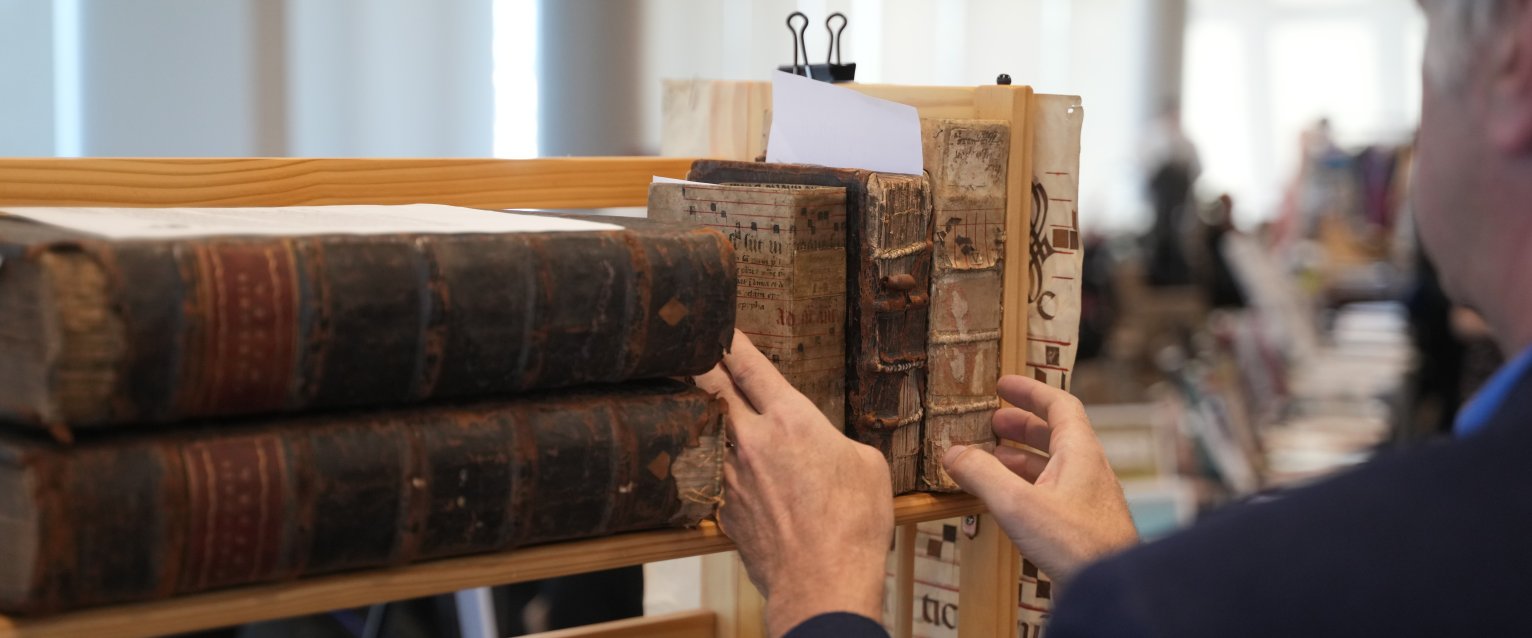 Person placing three books on a shelf. The books are old and have exposed bindings on the spines.