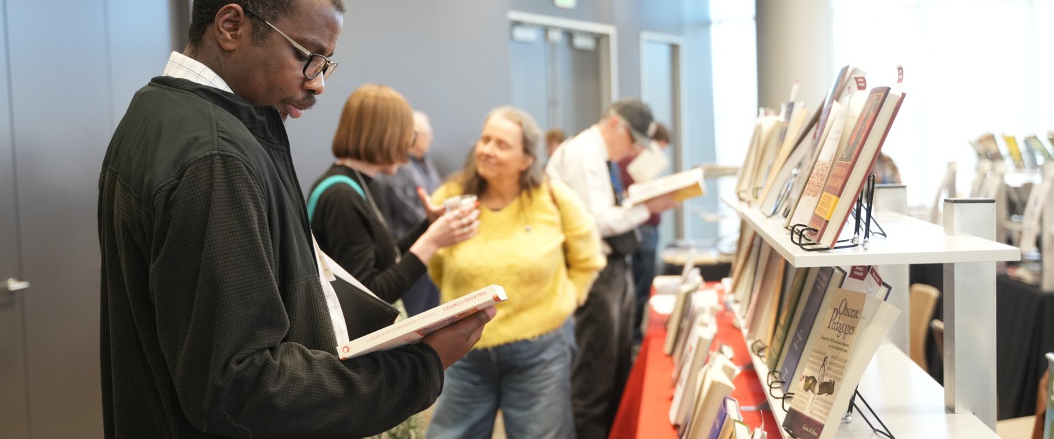 Person with short dark hair and wearing a black jacket reading a book. 