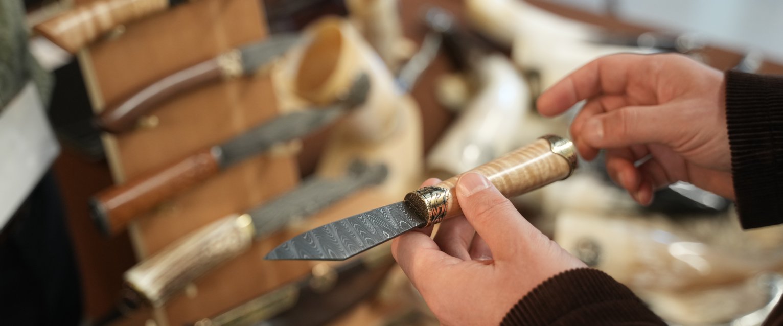 Person holding a small knife with a decorative blade and wooden handle.