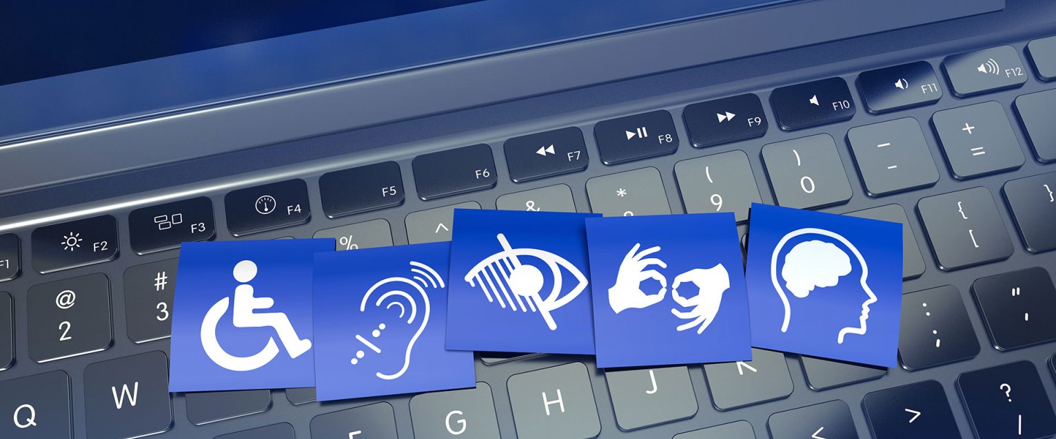 A computer keyboard with small printed sheets displaying accessibility icons, such as a wheelchair symbol and screen reader icon, placed on top.
