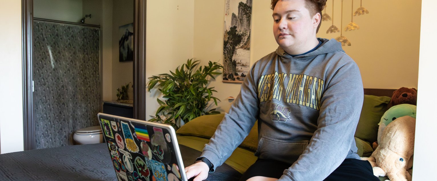 Student wearing a WMU sweatshirt studies in a decorated apartment bedroom
