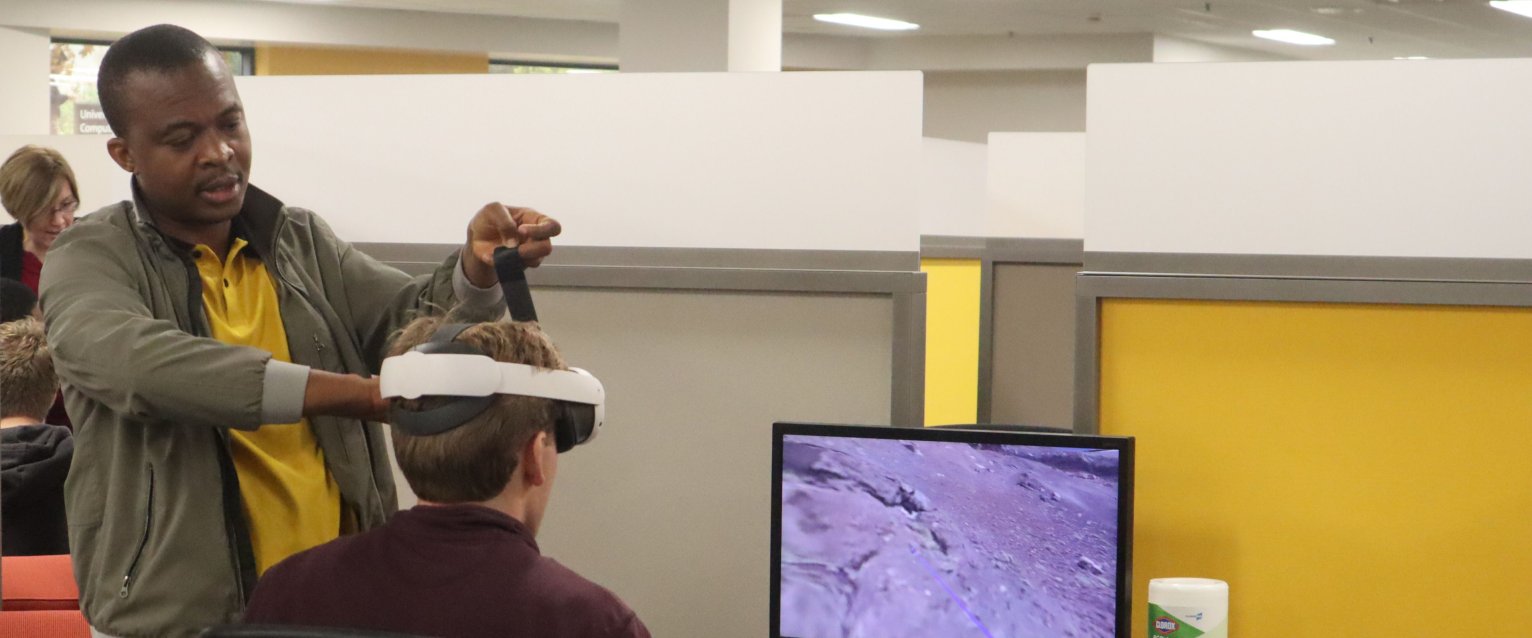 Fredrick Magi, a doctoral student in Science Education at Western Michigan University, assists a student with his VR headset during a geoscience course that combined 3D printing and virtual reality to help students learn about topography.
